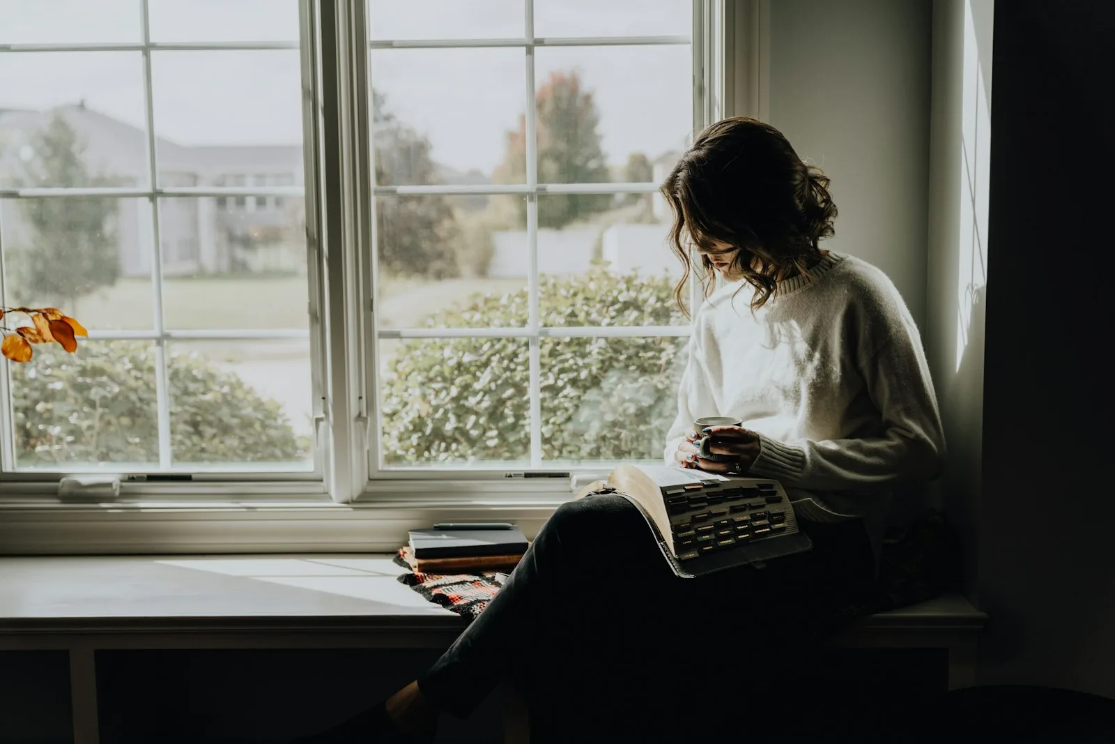 Mujer reflexionando junto a una ventana con un libro